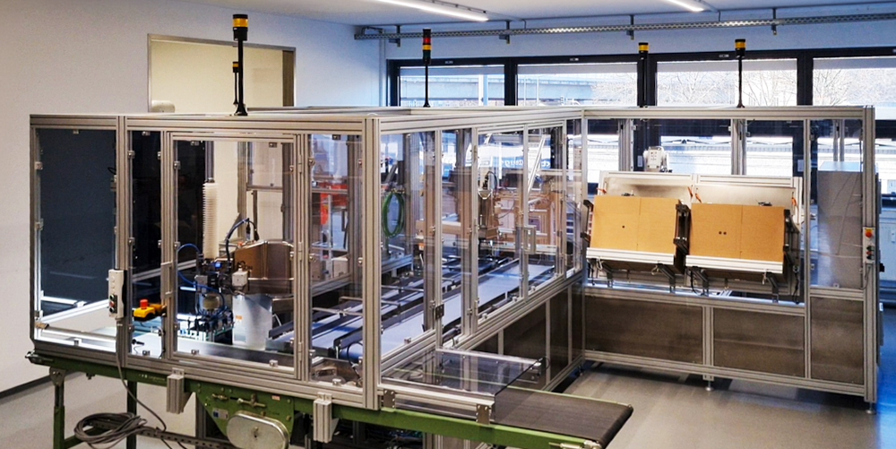 Verpackungs- und Palettieranlage mit Förderbändern, Einhausung und Roboterstationen.