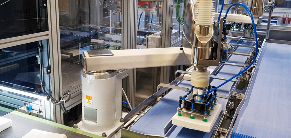Roboter mit Greifer nimmt einen Papierstapel auf einem Förderband auf.