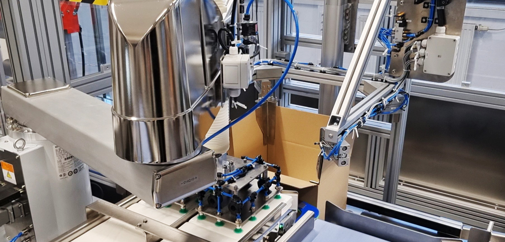 SCARA-Roboter mit Greifer setzt einen Papierstapel in einen Karton ein.