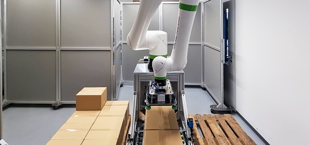 Kollaborativer FANUC-Roboter nimmt einen Karton für die Palettierung auf.